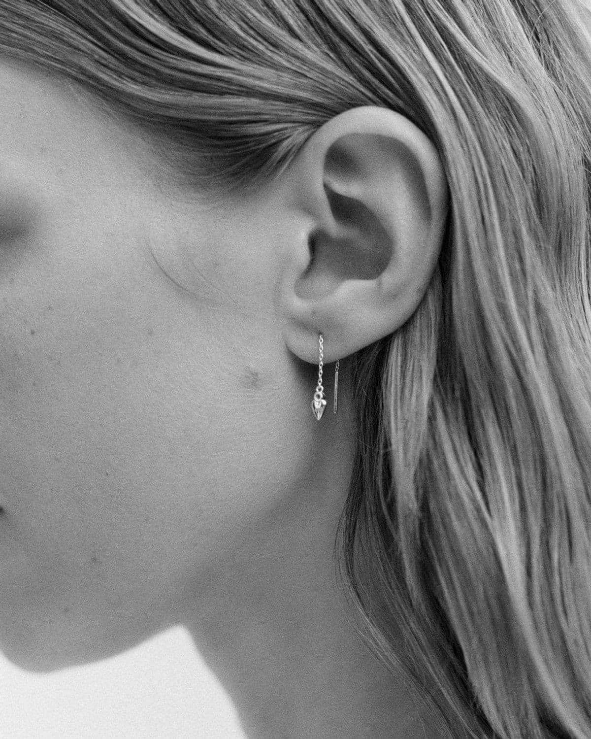 Black-and-white close-up of model's ear and jawline wearing a delicate threader drop earring, dreamy soft focus