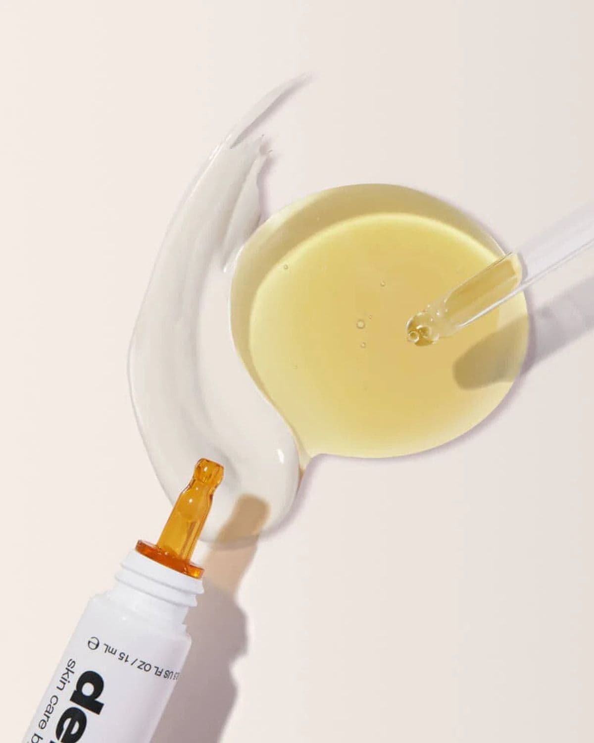 Abstract macro shot of a swirl of white cream and golden facial oil pooling together beside an open amber dropper bottle
