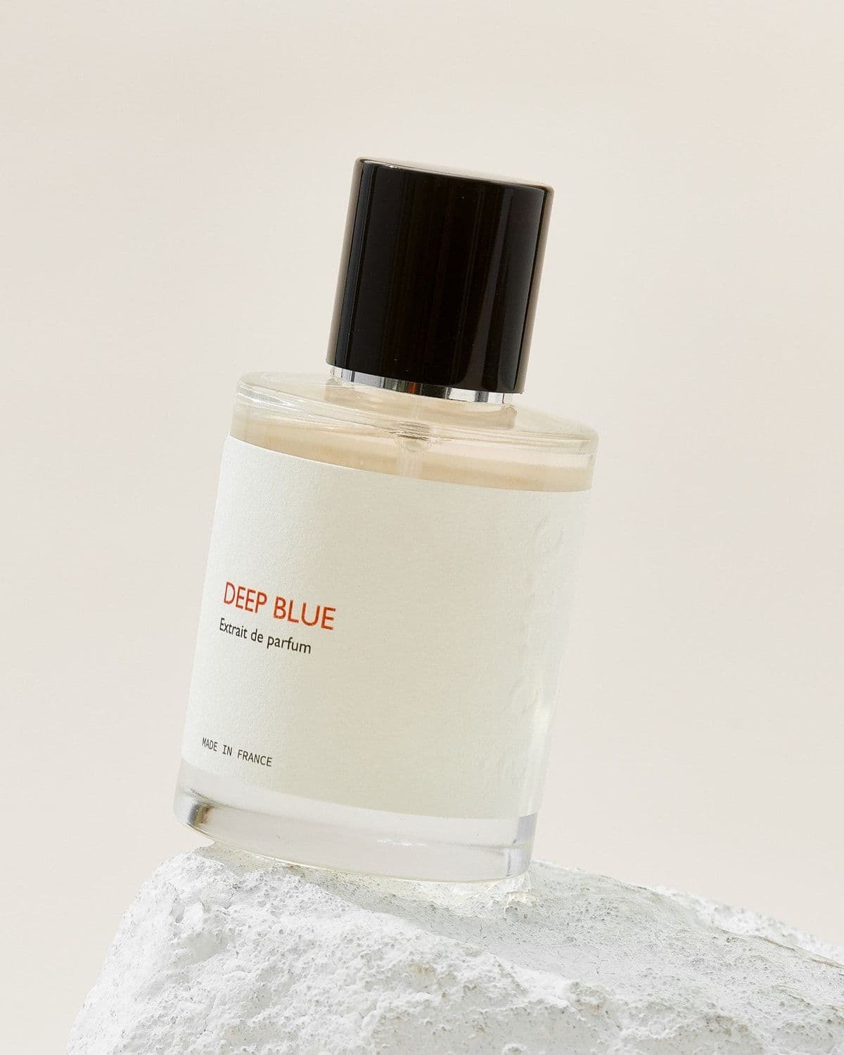 Àerre 'Deep Blue' perfume bottle perched on a pale porous stone with two lime wedges beside it, soft cream backdrop