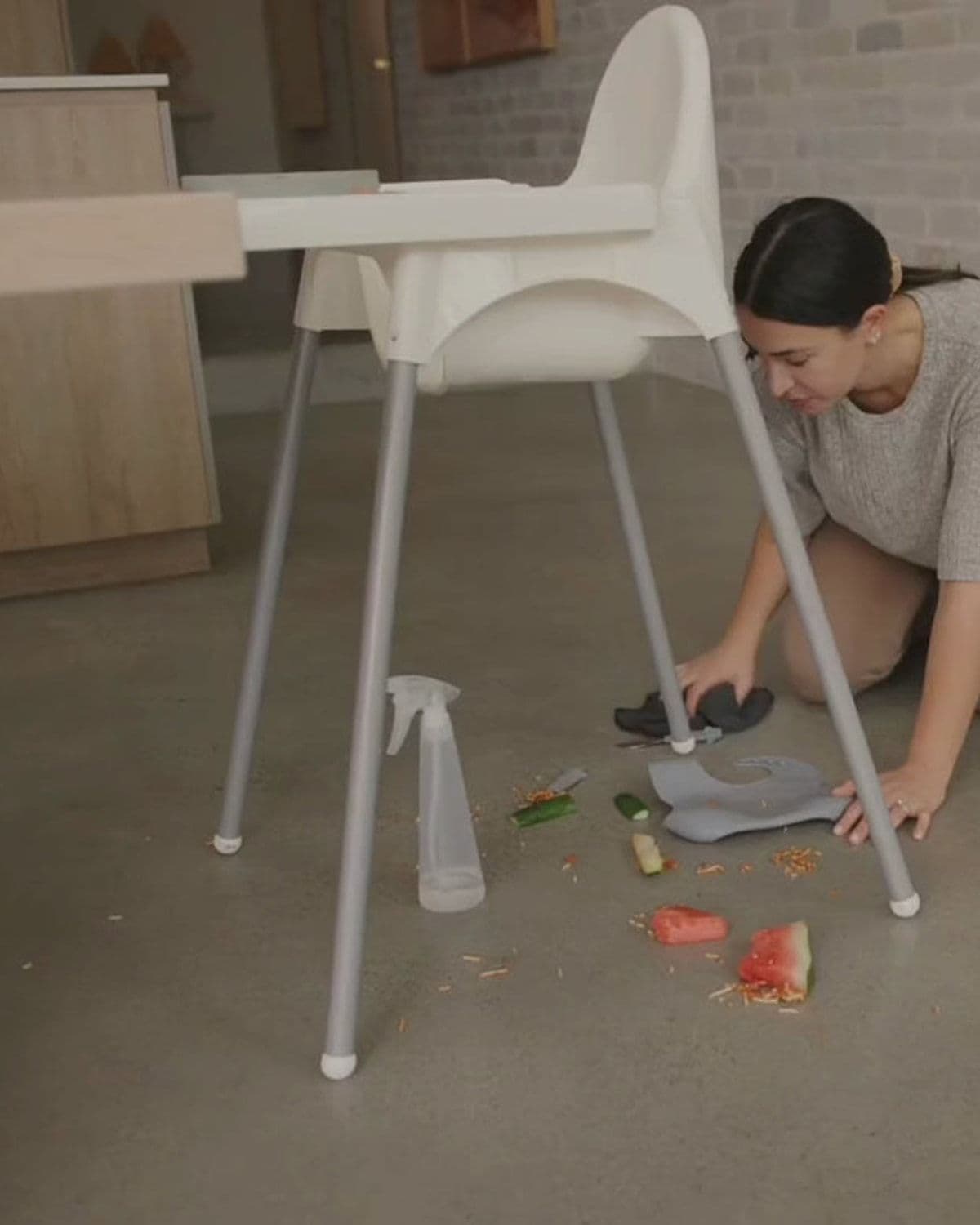 Parent kneeling to clean up dropped food from the floor beneath an IKEA high chair with Catchy tray installed