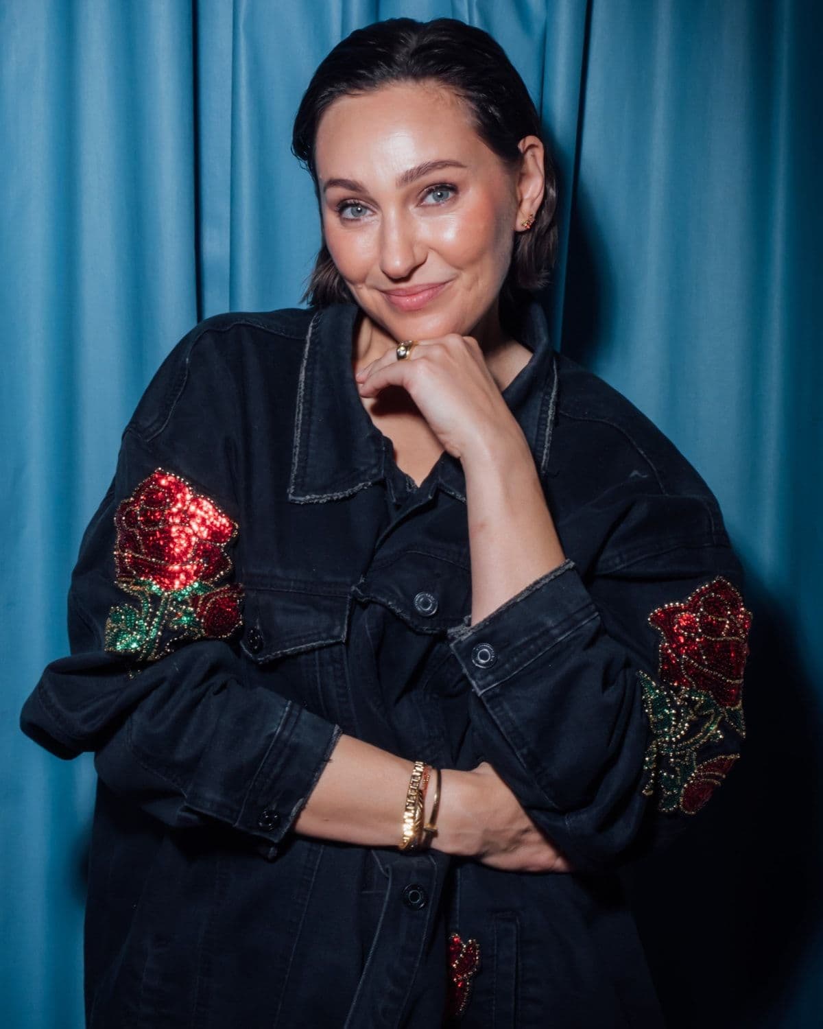 High-res founder studio portrait, blue curtain backdrop, rose-embroidered denim jacket