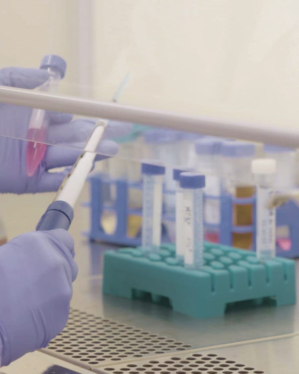 Close-up editorial shot of gloved hands using a pipette among lab test tubes and a sample rack, illustrating the brand's science-led formulation process