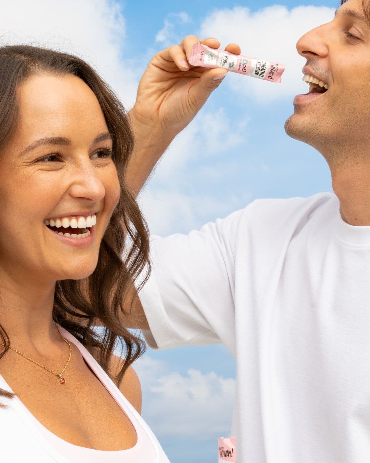 Couple outdoors against a blue sky, one feeding the other a NOWAY! Creatine Opti sachet stick