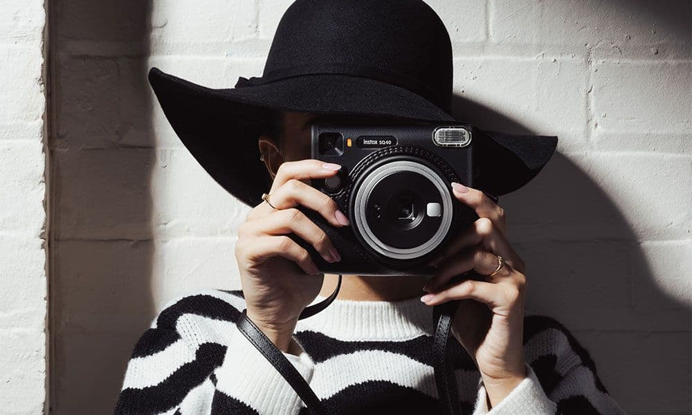 Person photographing with an Instax SQUARE SQ40 camera against a painted wall