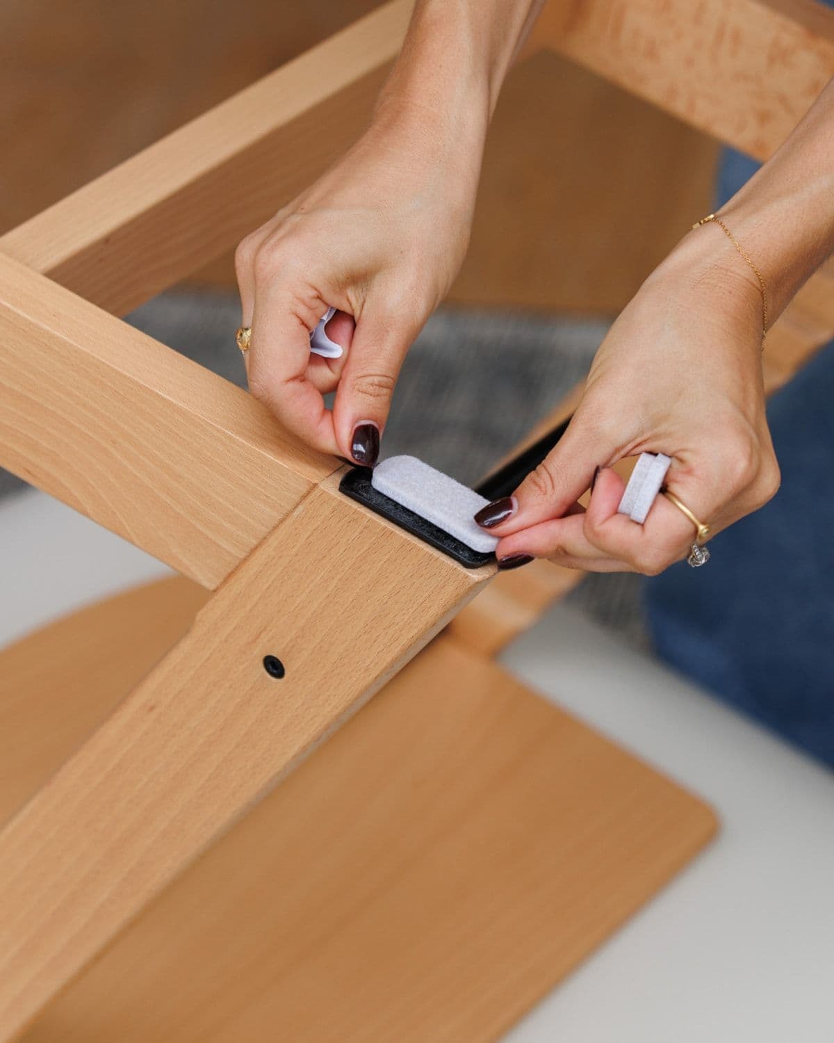 Close-up of hands installing Catchy floor-saver sliders onto wooden high chair legs