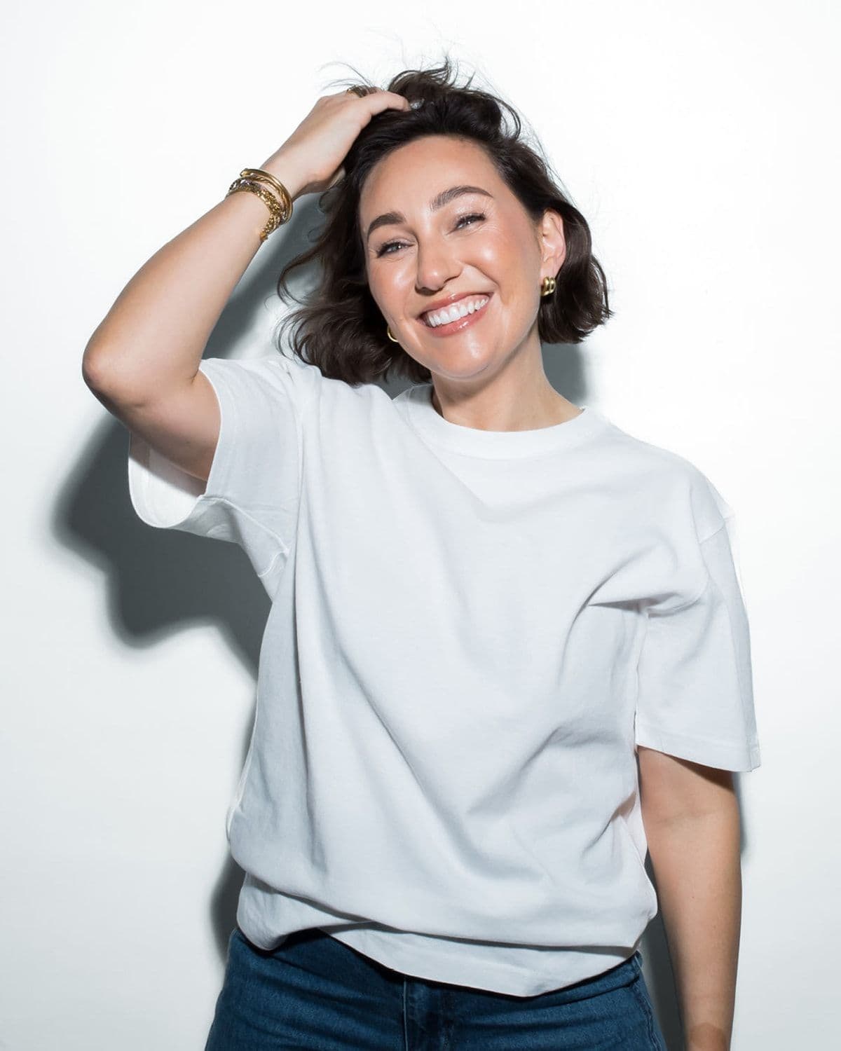 Go-To founder portrait, laughing, white tee, gold jewellery, studio white background (site nav 'Meet the Founder' tile)