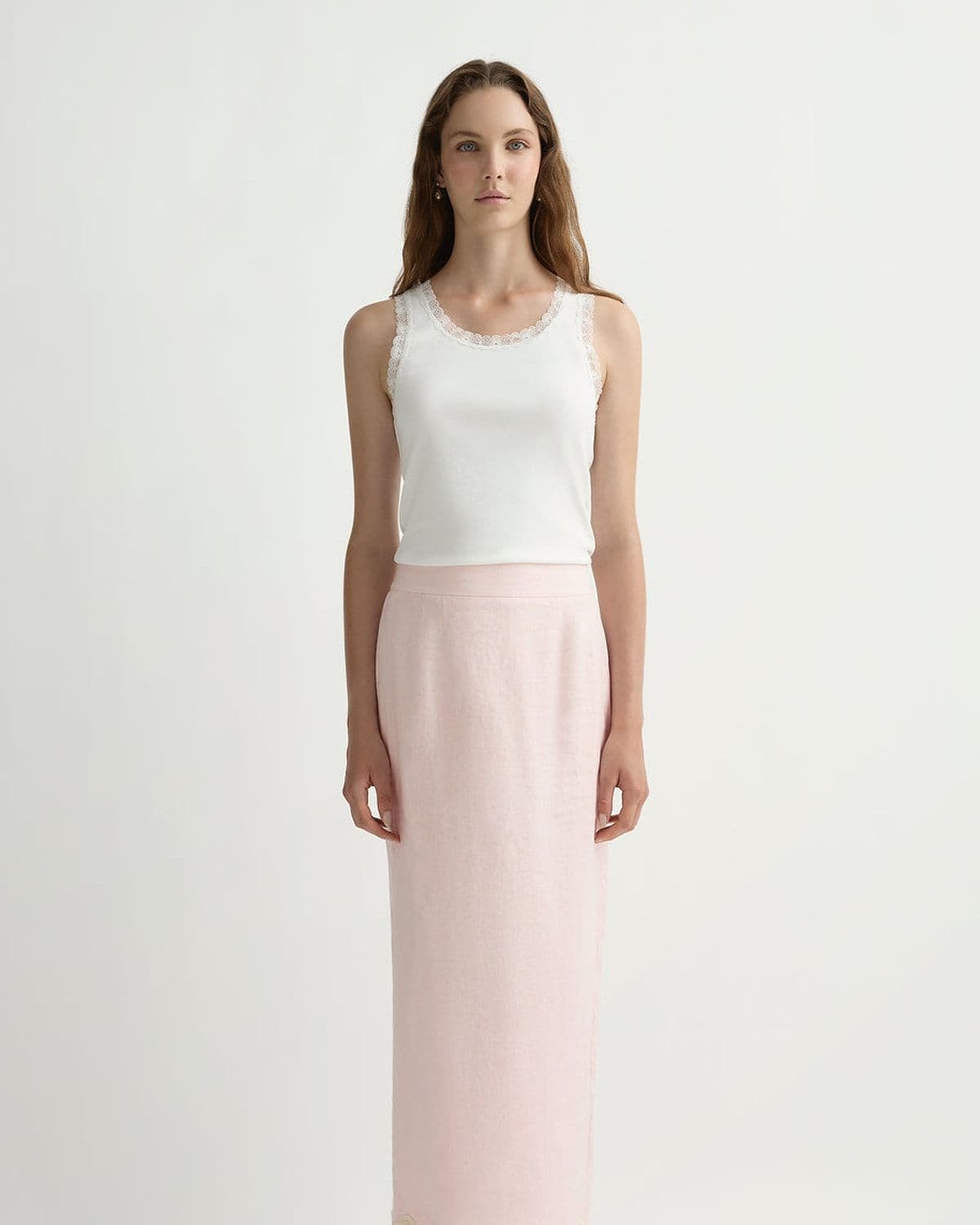 Model wearing a white lace-trim tank top and soft pink linen column skirt with a scalloped fringe hem, studio shot on white background