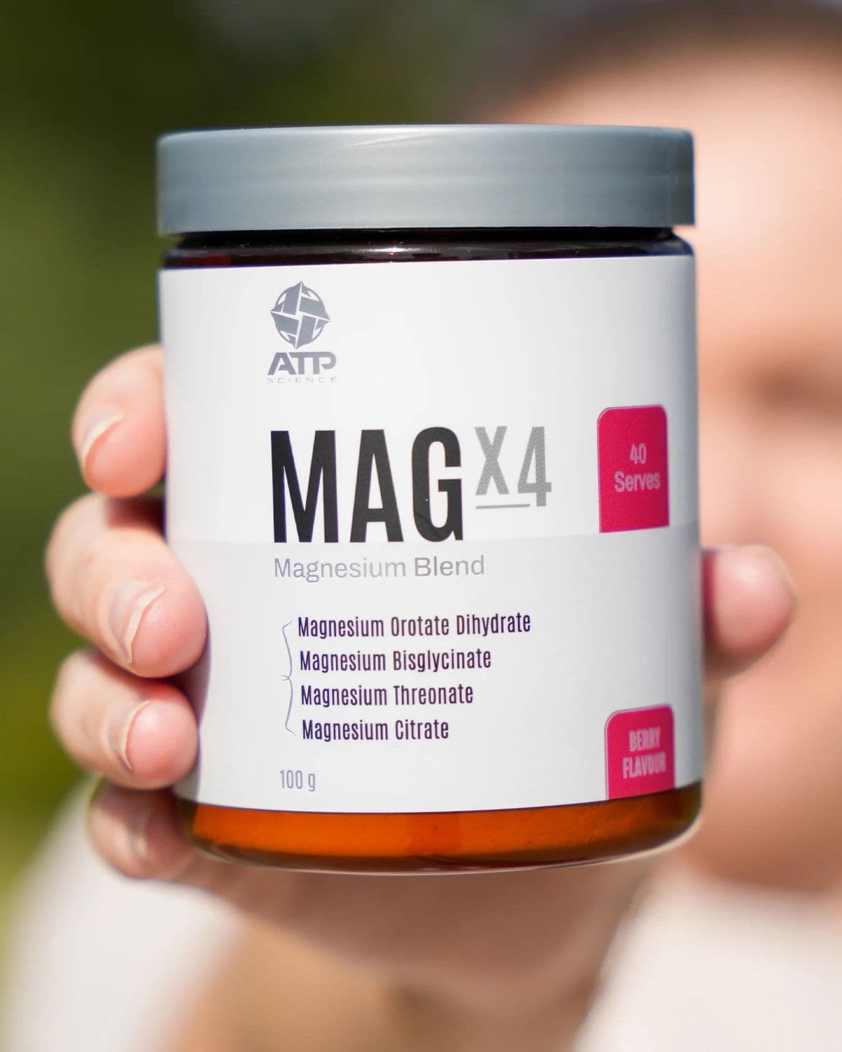 Hand holding a MAGx4 Berry magnesium jar outdoors with a blurred green background