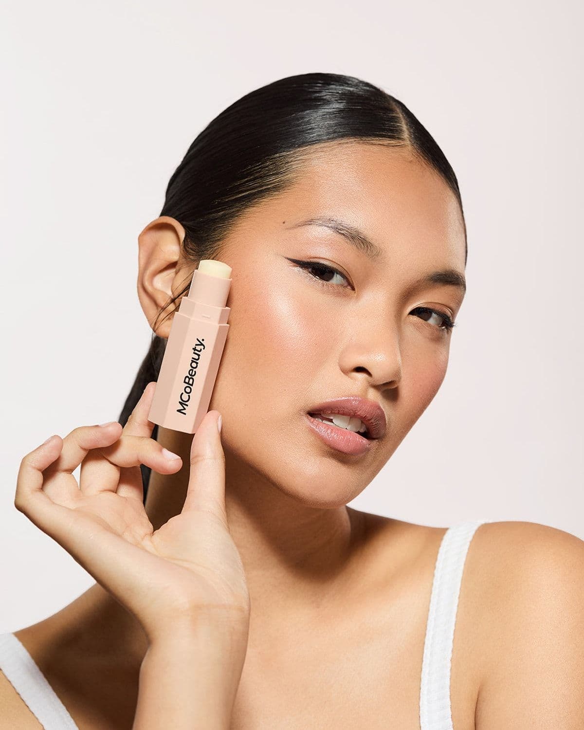 Smiling model holding an MCoBeauty lip balm stick in a warm-toned beauty portrait