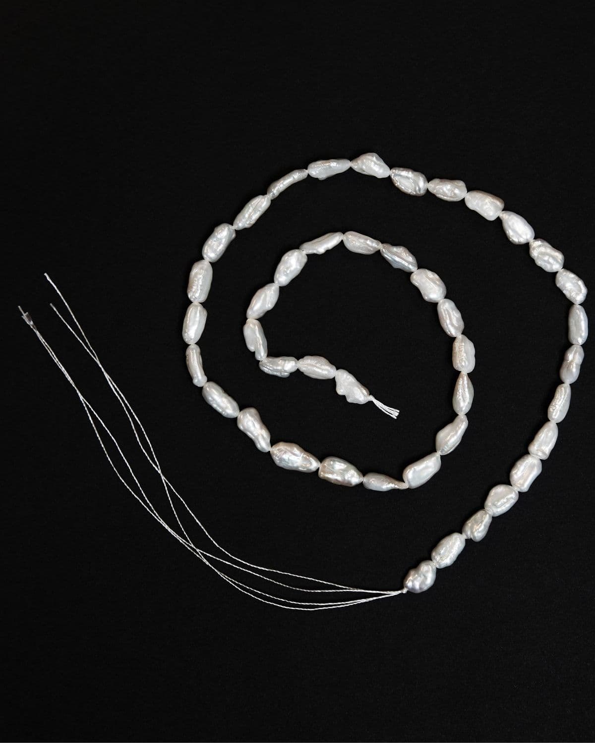 Loose freshwater pearl strands coiled on a black background, artisan product still life