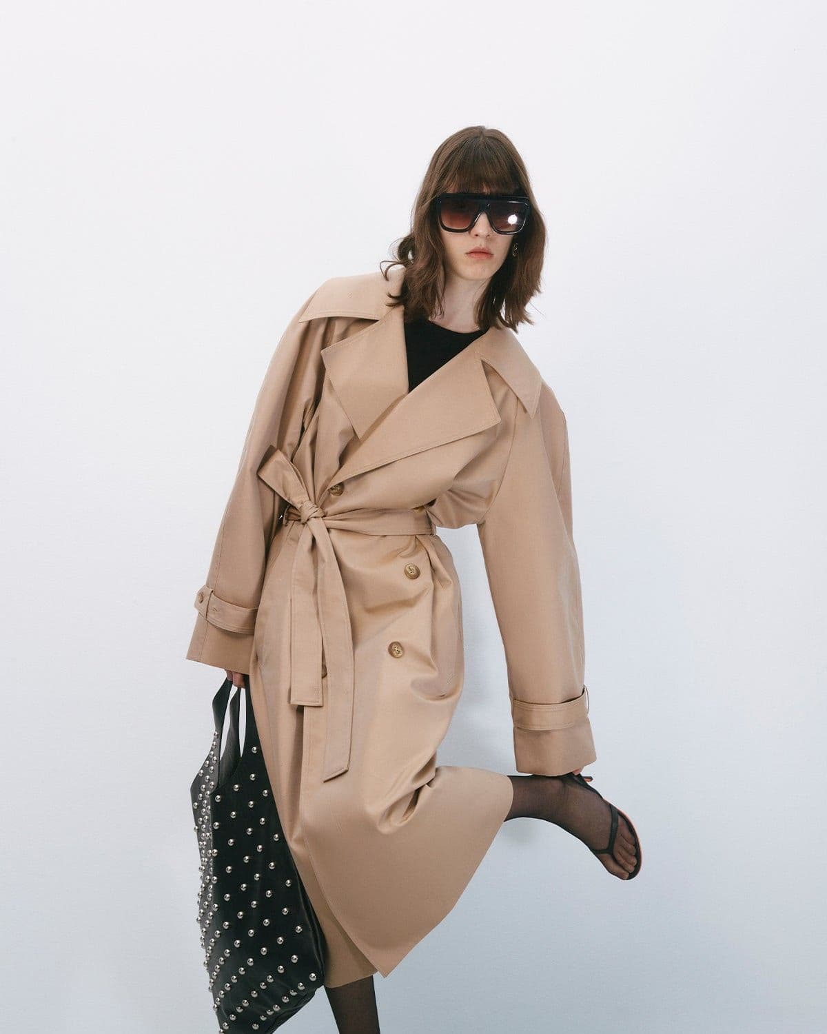 Model in a red, black and cream striped knit sweater and black wide-leg trousers, hand raised to shoulder, sunglasses, editorial pose