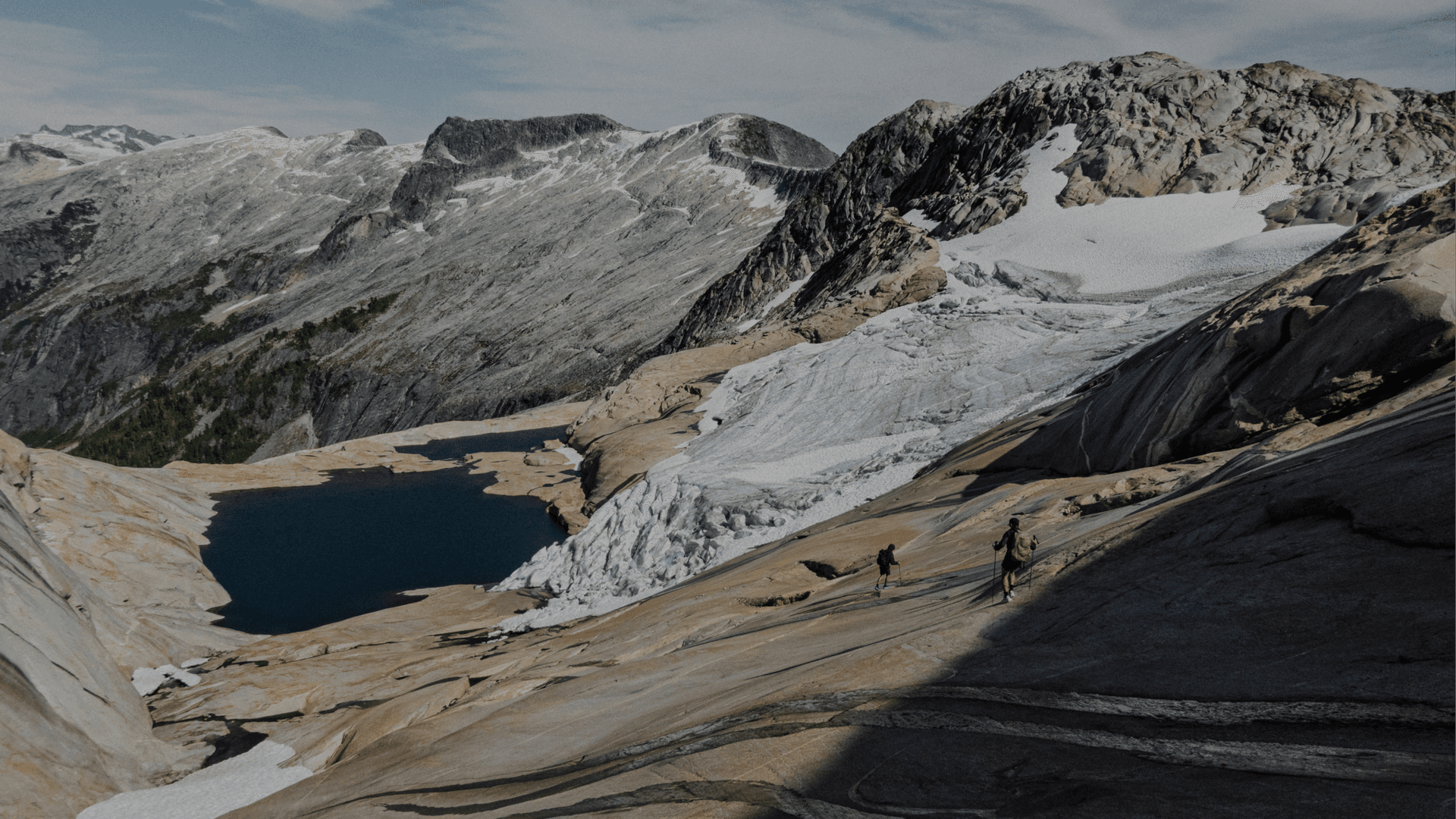 Two hikers crossing a granite slope above a glacial lake, from the official Arc'teryx campaign