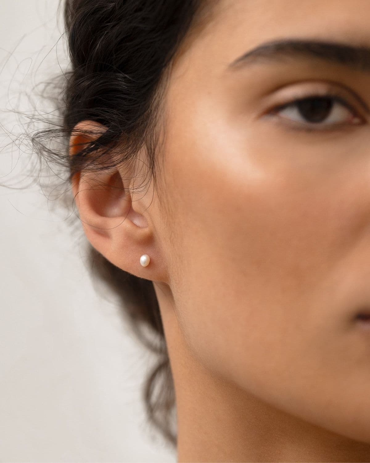 Close-up beauty shot of a woman's face and ear wearing a small pearl stud earring