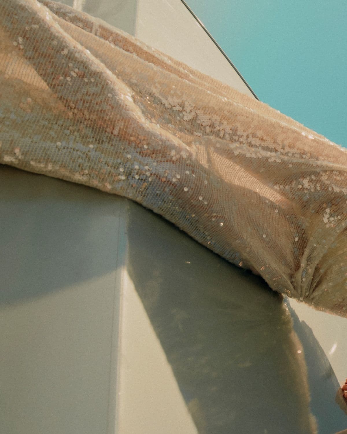 Model in sequinned gown leaning against architectural white structure, blue sky, Pre-Fall '26 campaign